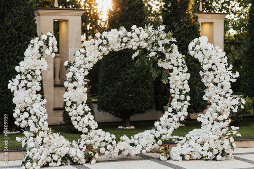 Obraz na płótnie Wedding ceremony outdoor. Arch, decorated with white flowers standing in the garden, in the wedding ceremony area. Arch for the wedding ceremony at sunset. w salonie