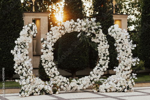 Obraz na płótnie Wedding ceremony outdoor. Arch, decorated with white flowers standing in the garden, in the wedding ceremony area. Arch for the wedding ceremony at sunset. w salonie