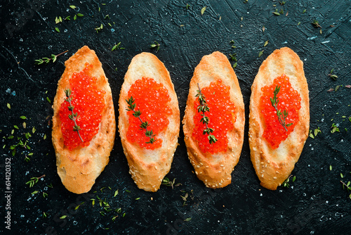 Toasts with red caviar on a stone plate, caviar in a bowl. On a black stone background. Rustic style.