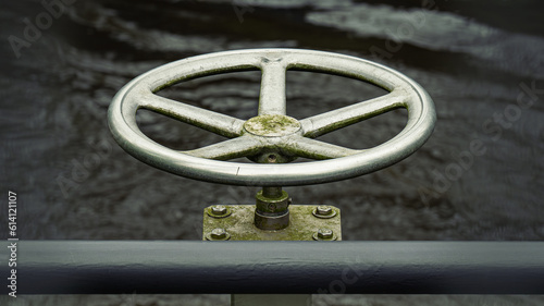 old silver steel steering wheel with dark water in the background as autonomy, decision making, direction, industrial concept with copy space and selective focus.