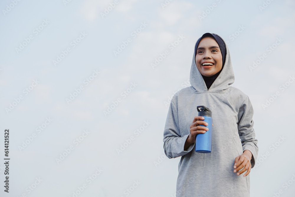 Fototapeta premium asian muslim woman running and exercising while holding drink bottle outdoors excitedly