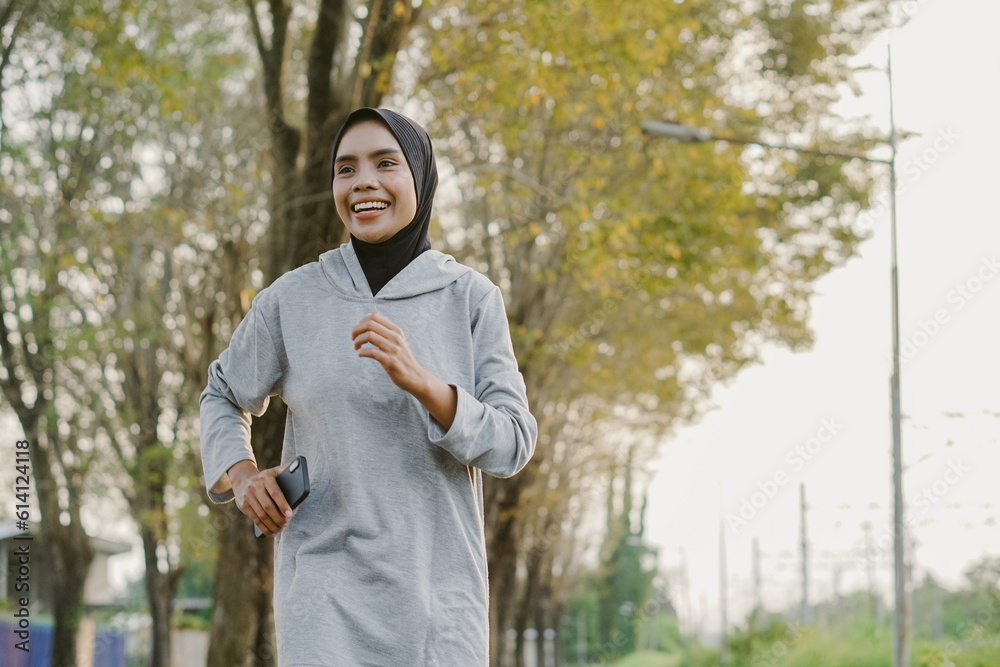 asian muslim woman running and exercising while holding mobile phone outdoors excitedly asian muslim woman running and exercising while holding mobile phone outdoors excitedly