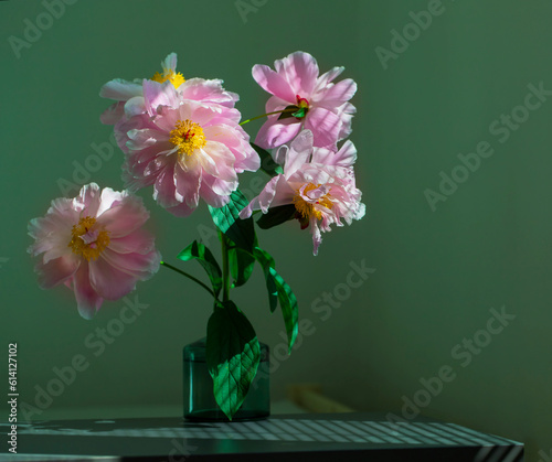 Bouquet of peonies in a glass vase on a green background.