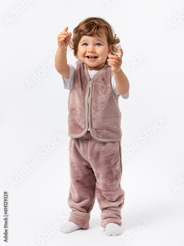 A cute baby 1-2 years old with curly hair and blue eyes asks for his hands, raising his hands up and looking expressively at a white background. Model. Copy space.