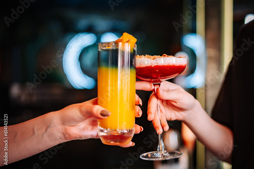 hands of two unknown women holding and clinking glasses cocktails in restaurant