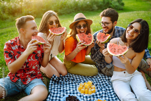 Young people eating watermelon on the picnic outdoors. People, lifestyle, travel, nature and vacations concept.