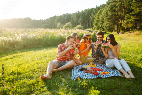 Young people eating watermelon on the picnic outdoors. People, lifestyle, travel, nature and vacations concept.
