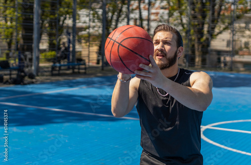 Athletic lebanese man in sportswear playing basketball game, successfully throws ball into the basket ring. Young guy on urban city summer court. Fitness routine on sports field. Motivation. Outdoors © Andrii Iemelianenko