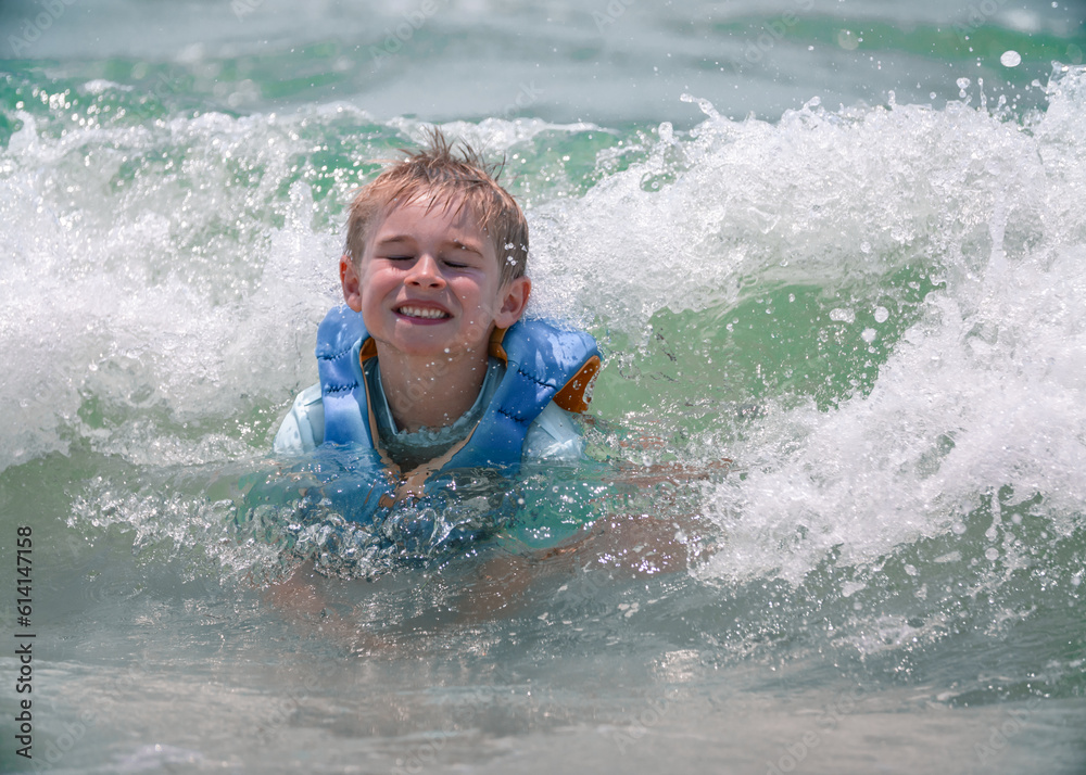 adorable smiling Young boy getting splashed by beautiful emerald water and waves at beach while vacationing in Mexico Beach, Florida