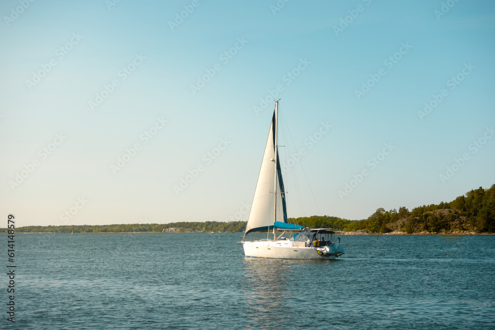 White sailboat sailing in calm water in summer sunset in Stockholm archipelago in Sweden