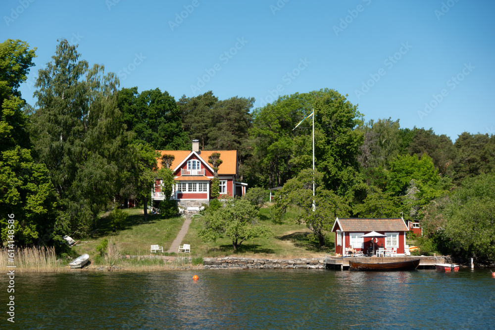 Obraz premium Typical Swedish red house with white trims by sea shore in idyllic summer landscape 