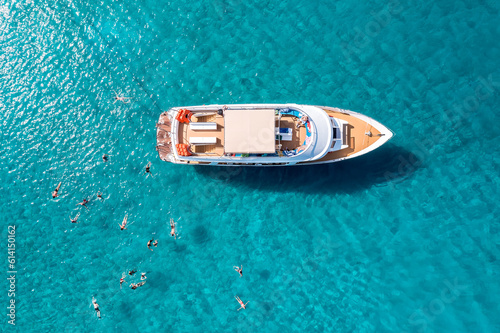Close-up overhead view of a yacht anchored in the turquoise sea and swimming tourists © kirill_makarov