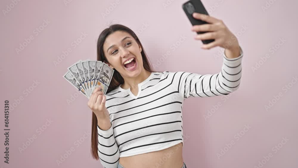 Young beautiful hispanic woman taking selfie holding dollars over isolated pink background Young beautiful hispanic woman taking selfie holding dollars over isolated pink background