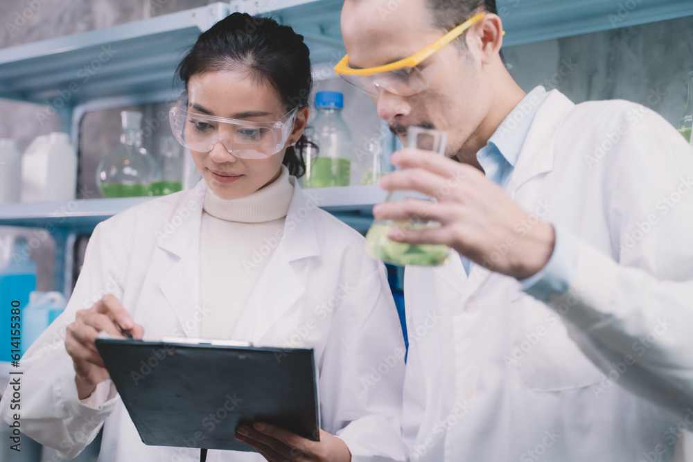 Young researcher woman is note on a pen in notebook and looking a simples liquid in tube at hand of a researcher man in the laboratory. Young researcher woman is note on a pen in notebook and looking a simples liquid in tube at hand of a researcher man in the laboratory.