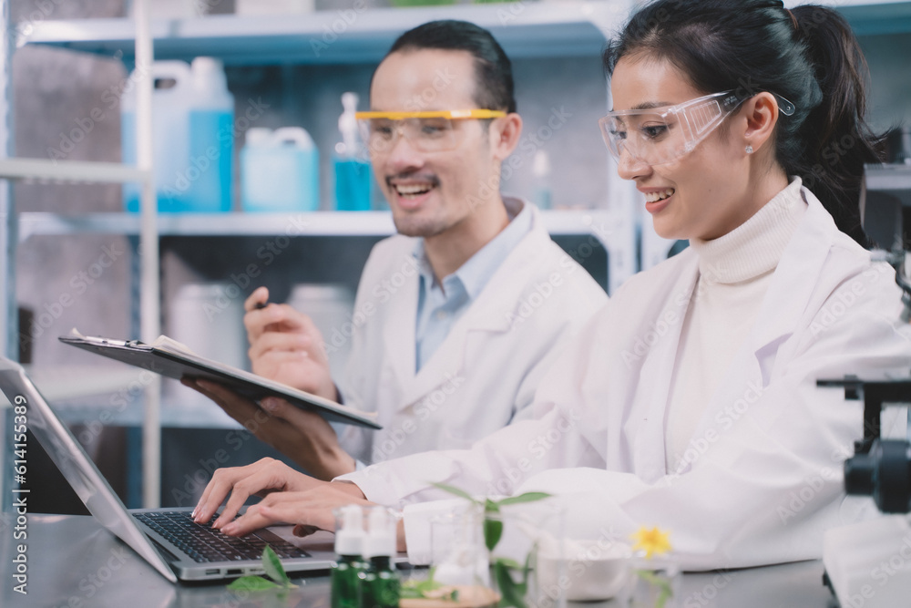 Fototapeta premium Two researchs people are save data to labtop and research man is making notes on a pen in his notebook in a laboratory at a table