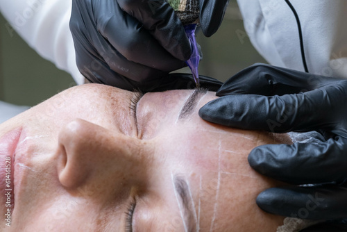 Close-up of microblading process: art of eyebrow tattooing. With gloved hands, skilled practitioner wields aspecialized needle, embedding pigment into skin. eyebrows are meticulously tinted using