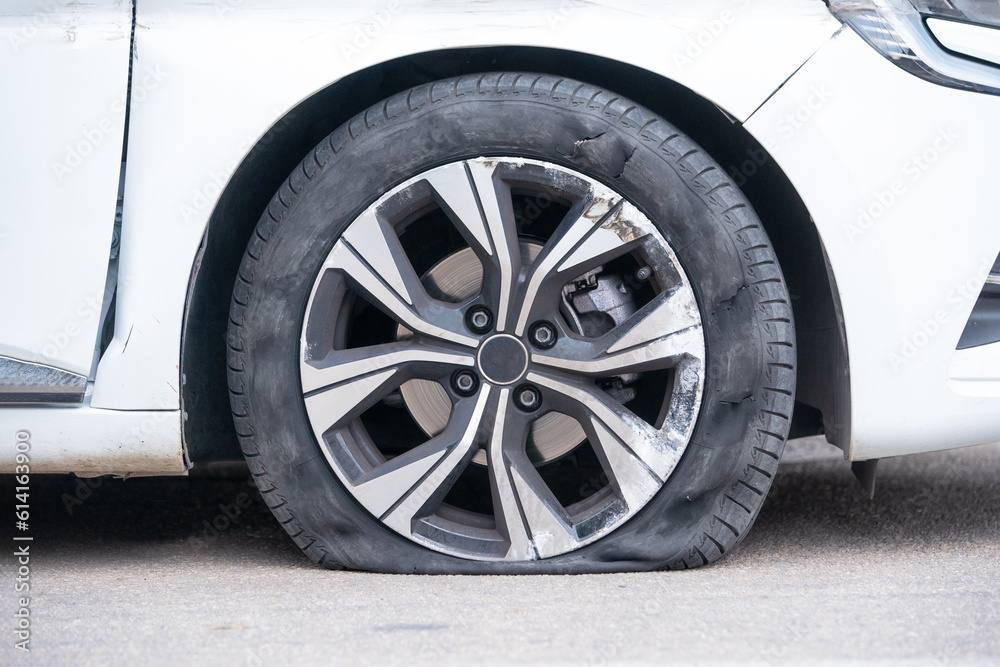 Close-up of flat right front wheel of car standing on road with alloy disc. Forced emergency stop on the side of roadside, burst tire, insured event. Broken car waiting tire shop, tire repair service Close-up of flat right front wheel of car standing on road with alloy disc. Forced emergency stop on the side of roadside, burst tire, insured event. Broken car waiting tire shop, tire repair service