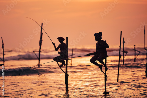 Fotografie Silhouettes of two traditional fishermen against ocean at dusk