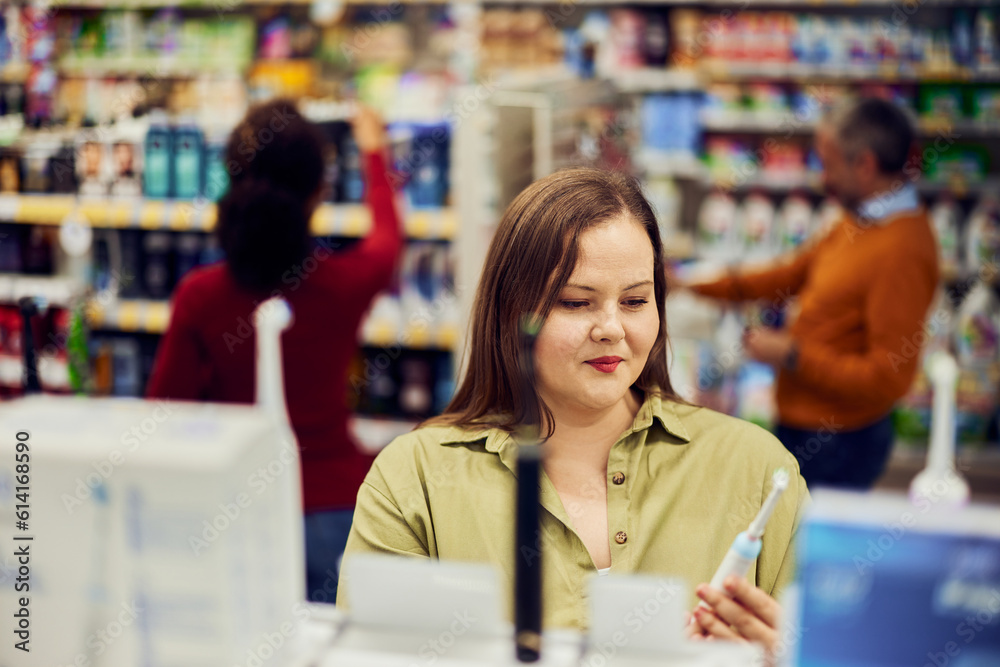 A pretty plus-size woman holding an electric toothbrush in a supermarket.