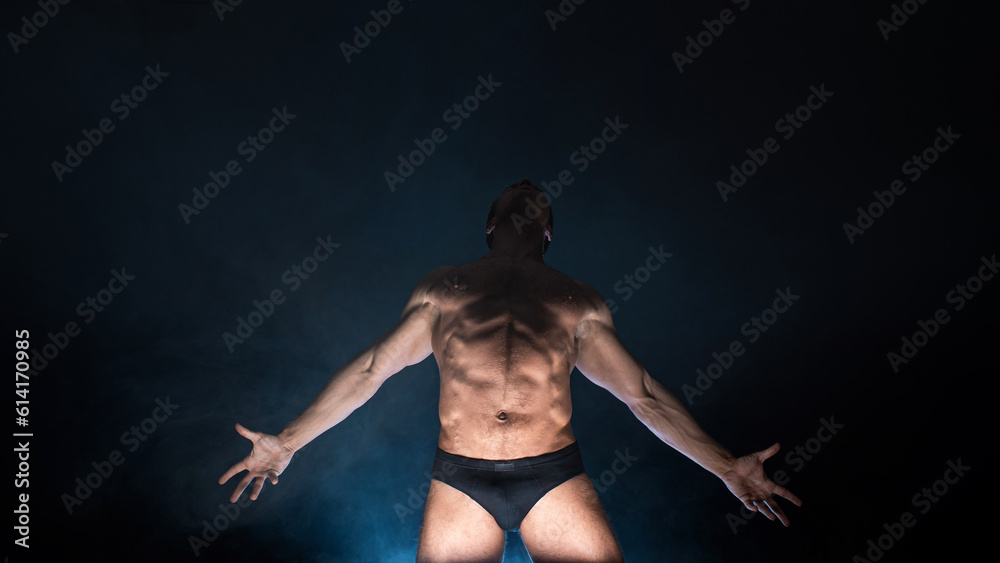 Obraz premium Muscular athlete in an epic pose, dark background, bright light from below, the concept of sports and bodybuilding