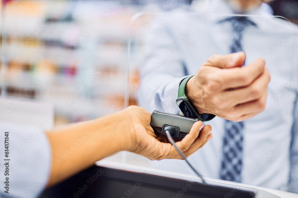 A close-up of a male with a smartwatch paying a bill at the counter in a store.