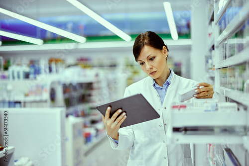 A busy female pharmacist using a tablet to do medical inventory at the drugstore.