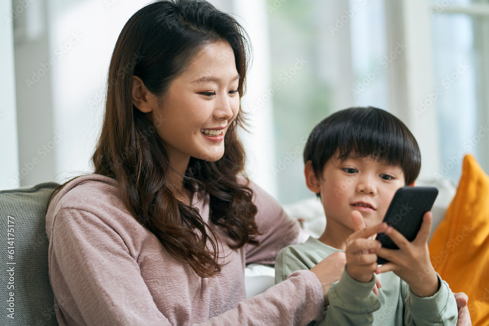 young asian mother sitting on family couch at home sharing cellphone picture content with son young asian mother sitting on family couch at home sharing cellphone picture content with son