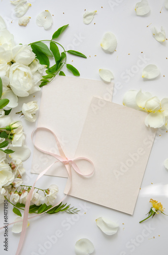 Delicate composition of blank card with white roses and petals with acacia flowers and pink ribbon on white background. Wedding concept. Invitation card template