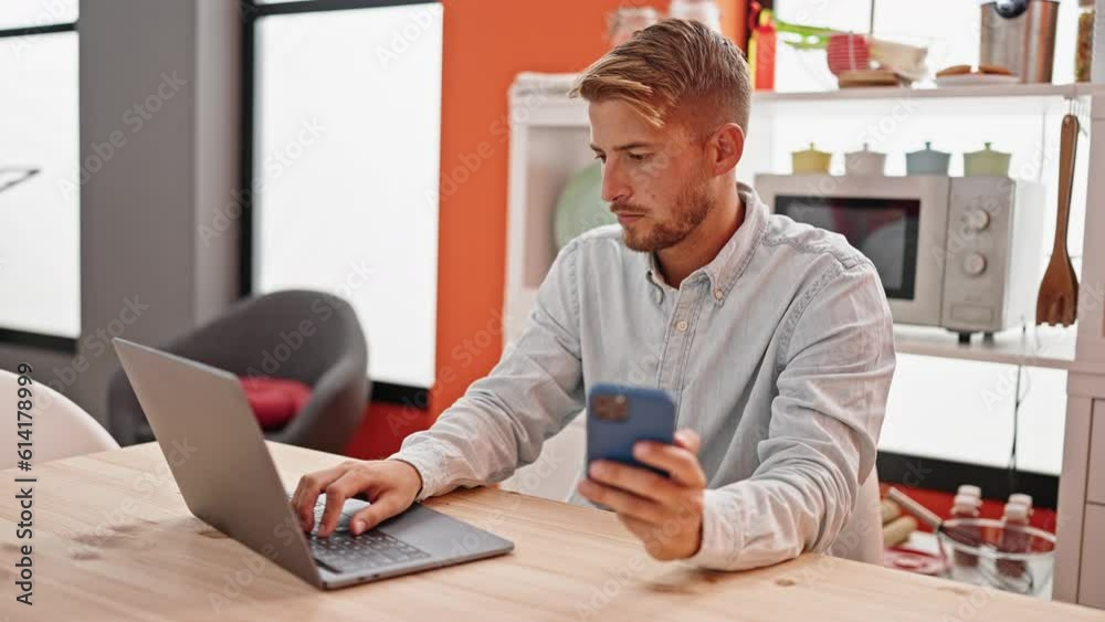 Young caucasian man using laptop and smartphone sitting on table at dinning room Young caucasian man using laptop and smartphone sitting on table at dinning room