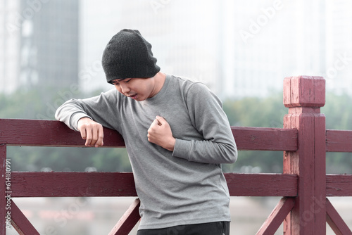 Asian man is covering his heart painfully outdoors, concept of sudden heartache after doing exercise. 