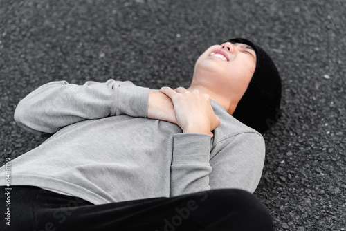 Asian young man lying on the ground, hand covering his heart, concept of sudden heart attack or carditis. 