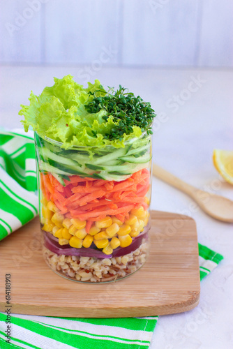 Healthy homemade salad with bulgur and vegetables in mason jar on wooden board with green napkin. Placed on white background. Selective focus