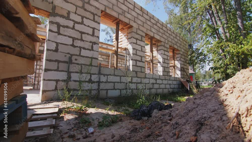 Foam concrete blocks carcass of building and supplies at construction site. Sand and wooden pallets next to brick house in wood Foam concrete blocks carcass of building and supplies at construction site. Sand and wooden pallets next to brick house in wood