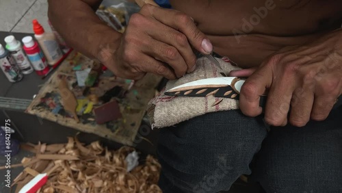 on the street man with beard of Indian appearance first people of Canada locals carving feather Poor people poverty close-up details of his work sawdust hands creativity crafting Vancouver Canada 2023