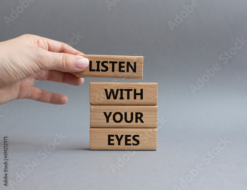 Listen with your eyes symbol. Concept word Listen with your eyes on wooden blocks. Beautiful grey background. Businessman hand. Business and Listen with your eyes concept. Copy space