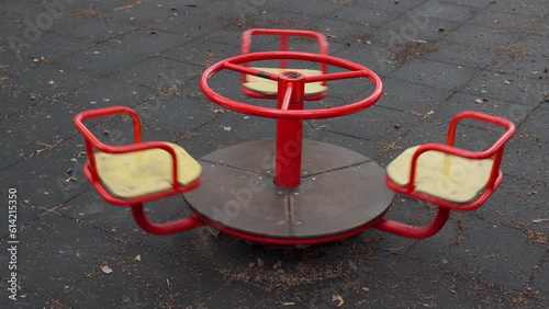 An empty red children carousel spins in a city park after rain close up. Lonely swing is spinning on the playground in the yard. Old deserted playing field without children. Video footage in 4k 25FPS photo