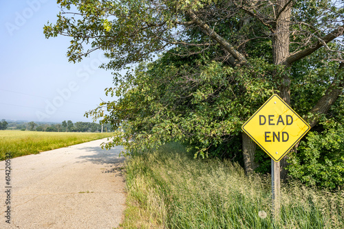 Dead end sign in front of trees along a narrow, country road. photo