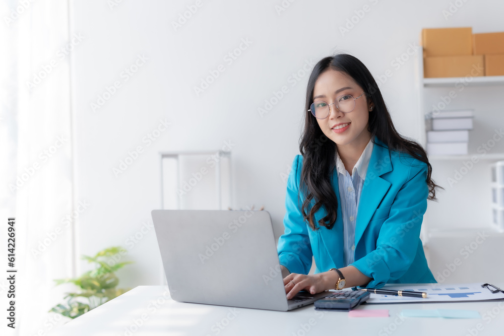 Happy smiling Asian businesswoman using laptop computer in the office. Beautiful young Asian female shopping or chatting online in social networks, freelance working on laptop projects.