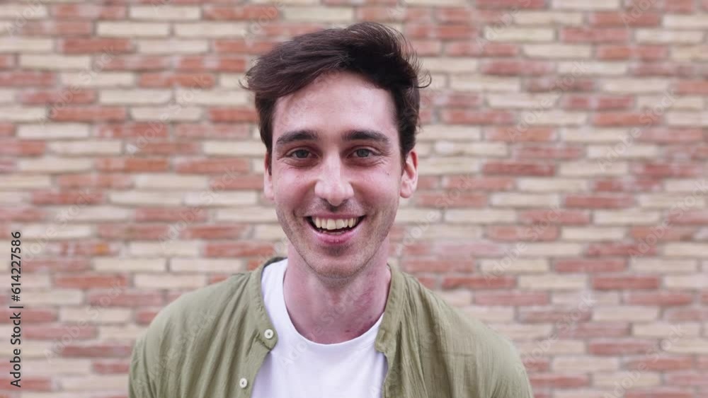 Portrait of young adult man smiling at camera standing over city wall background. Cheerful millennial male feeling positive. People concept. Portrait of young adult man smiling at camera standing over city wall background. Cheerful millennial male feeling positive. People concept.