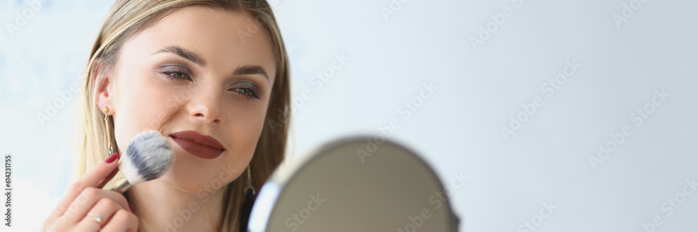 Smiling young woman looks in the mirror and paints herself with blush brushes. Makeup artist girl doing makeup learning with beauty and cosmetics video tutorials Smiling young woman looks in the mirror and paints herself with blush brushes. Makeup artist girl doing makeup learning with beauty and cosmetics video tutorials