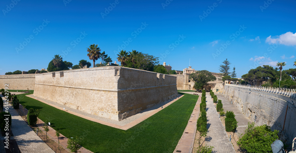 Ancient hilltop fortified capital city of Malta, The Silent City, Mdina or L-Imdina, skyline against blue Spring skies with huge walls, cathedral domes and towers, fields of spring flowers