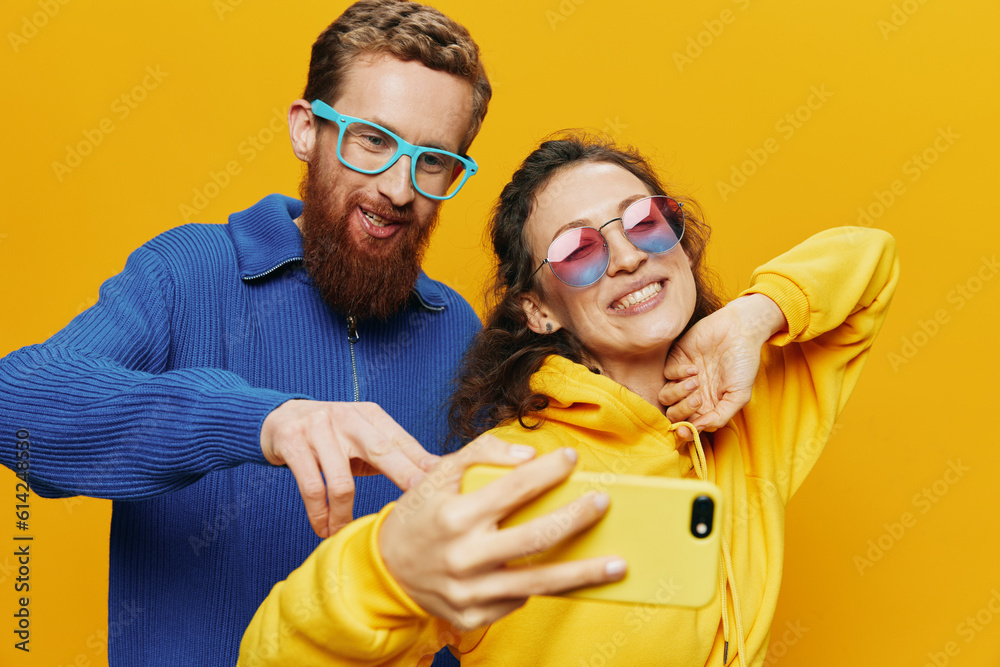 Obraz premium Woman and man funny couple with phones hand social networking and communication crooked do selfies smile fun, on yellow background. The concept of real family relationships, freelancers, work online.