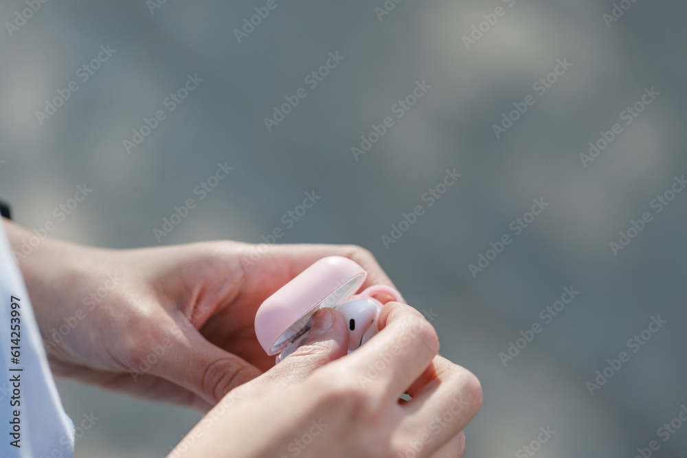 Close up of a woman hands taking off earbuds from case walking in the street