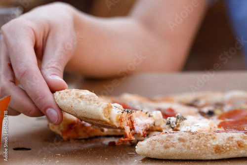Young happy caucasian woman sitting at table eating freshly baked pizza and drinking fresh in outdoor cafe on clear sunny summer day