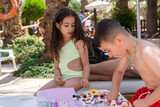 Two Children Enjoy a Playful Afternoon by the Pool. Curly- Haired Girl and Her Brother Engage in Constructing Structures Using Building Blocks, Fostering Imagination in the Summertime Ambiance.