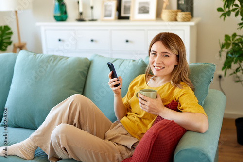 Woman using smartphone while drinking coffee at home in the morning