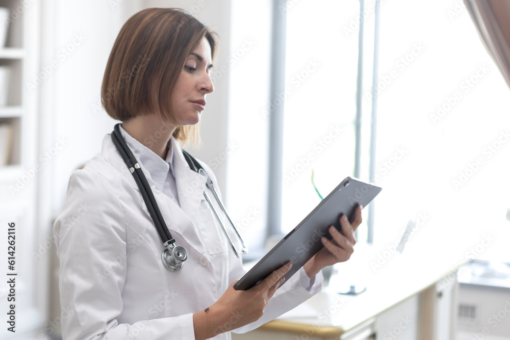 Side view on female physician standing and holding gadget and documents of patients. Modern health care concept Side view on female physician standing and holding gadget and documents of patients. Modern health care concept