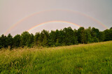 Double rainbow above the forest and meadow. Sunny and rainy weather at the same time caused this rare phenomenon. Spring evening in Czech republic.