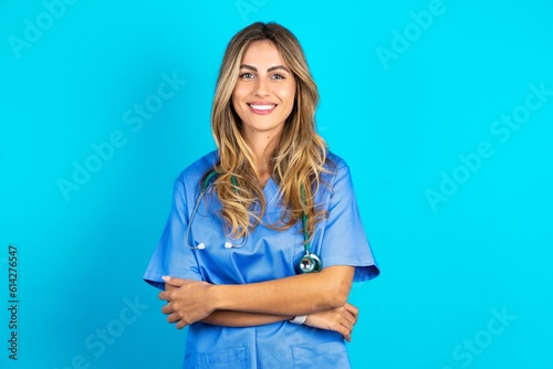 Close up photo of Young beautiful doctor woman standing over blue studio background toothy smiling