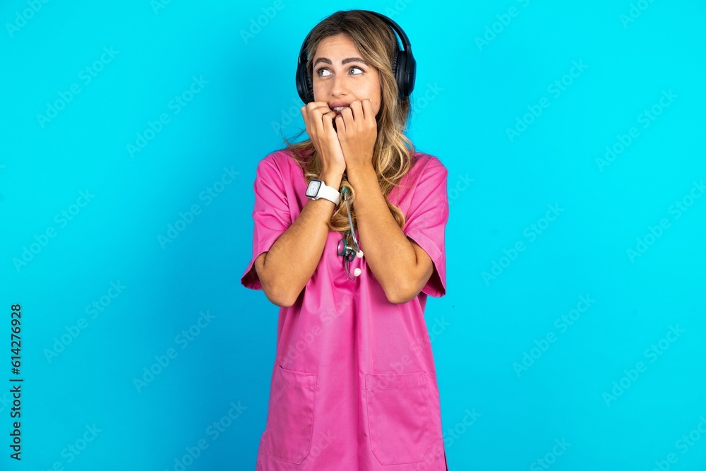 Terrified Young beautiful doctor woman standing over blue studio background looks empty space home alone moonless night Terrified Young beautiful doctor woman standing over blue studio background looks empty space home alone moonless night